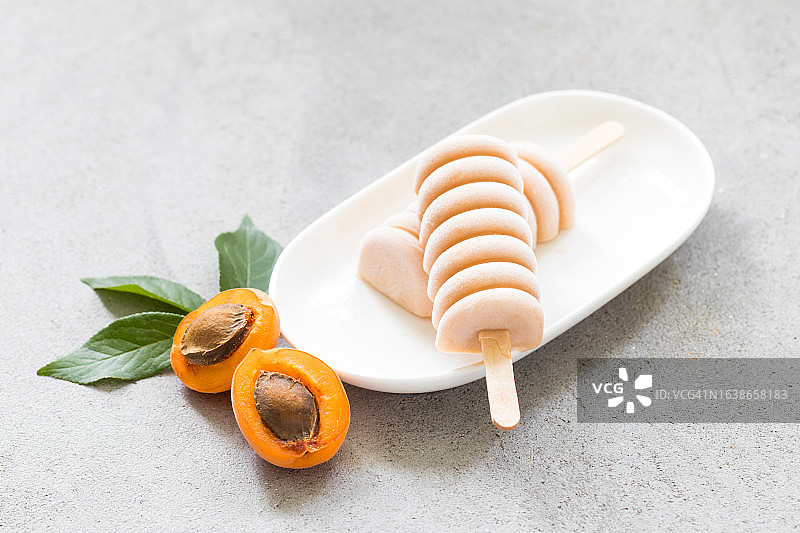 盘中木棍上的杏子冰淇淋，浅灰色背景，特写图片素材