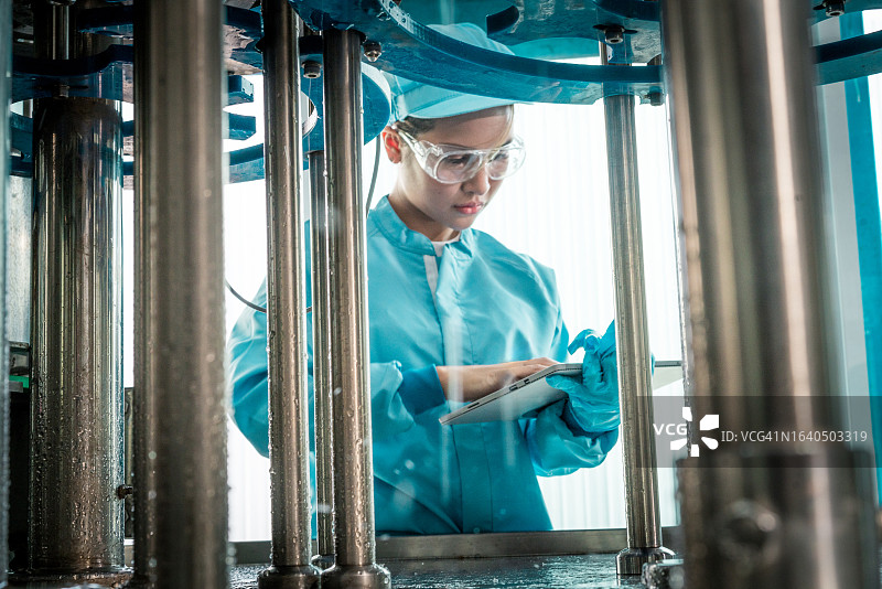 年轻女工在饮料厂使用平板电脑检查传送带上的产品，检查装瓶生产线，进行质量控制图片素材