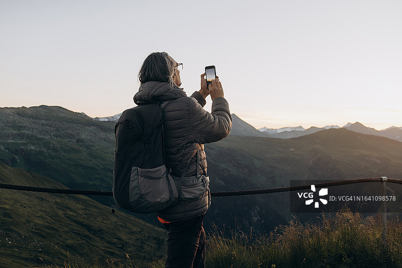 老年男人用智能手机拍摄山中日落并发布到社交网络上图片素材