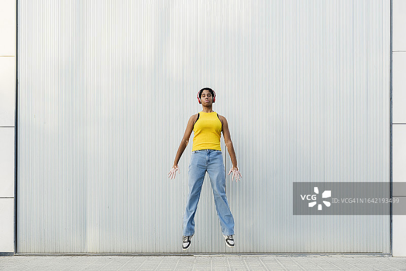 戴耳机在灰色背景前跳跃的少女图片素材