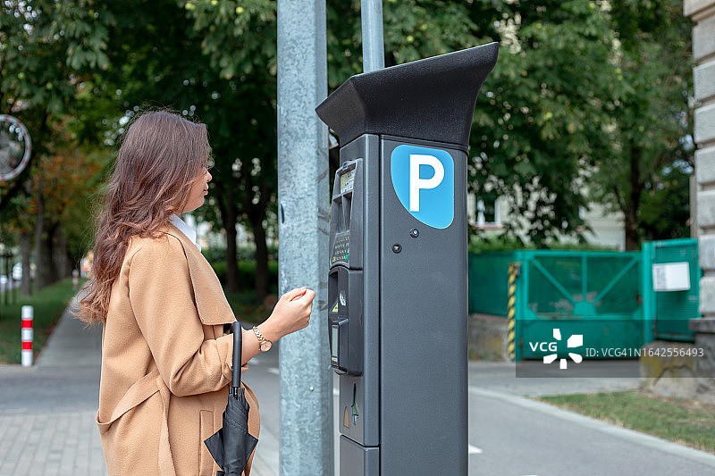 穿着时髦的美丽年轻女子走向街上的停车收费表的侧视图图片素材