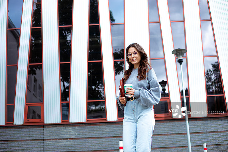 优雅年轻女人拿着平板和咖啡杯走在校园建筑前图片素材