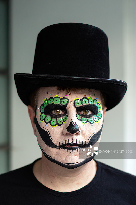 在墨西哥城亡灵节庆祝活动中，脸上画着糖骷髅并戴着高顶礼帽的中年男人肖像图片素材