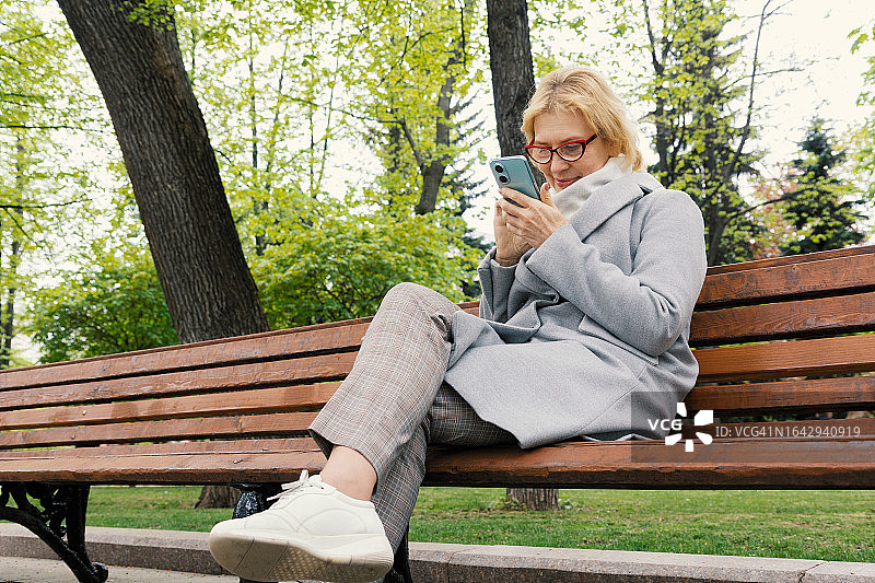 公园里穿着外套用手机放松的中年妇女图片素材