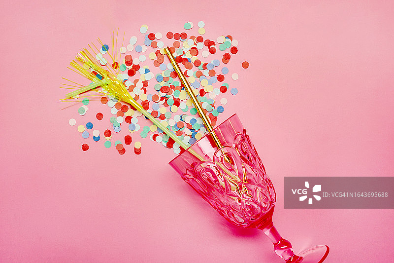 粉色背景上的玻璃杯、吸管和五彩纸屑图片素材
