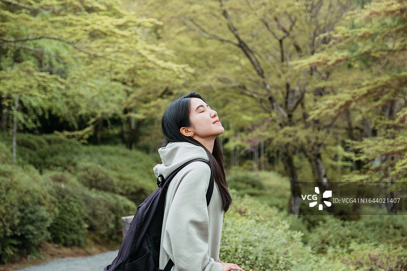 微笑的年轻漂亮的亚洲女子闭着眼睛在日本奈良的自然公园呼吸新鲜空气。放松、旅行、休闲和度假的概念图片素材