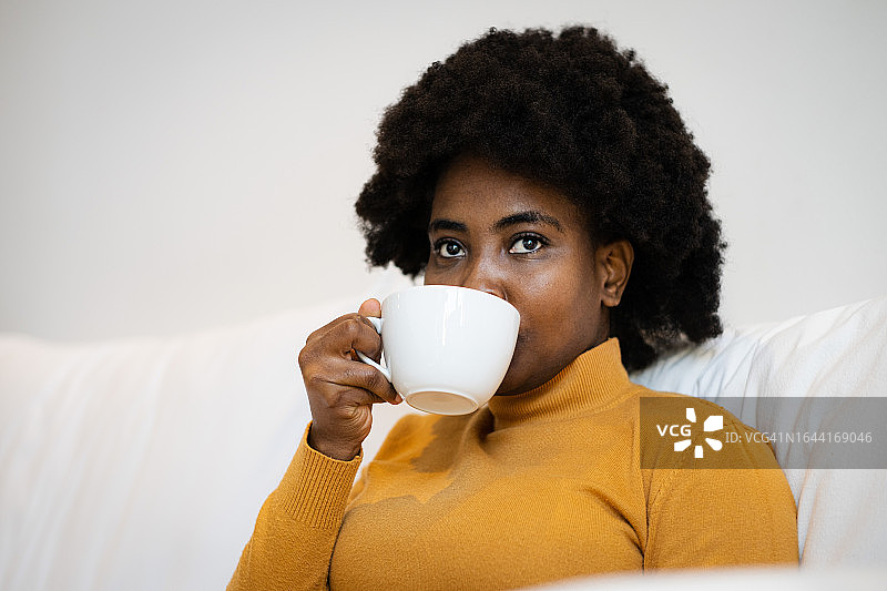 在沙发上喝咖啡的深思熟虑的年轻女子图片素材