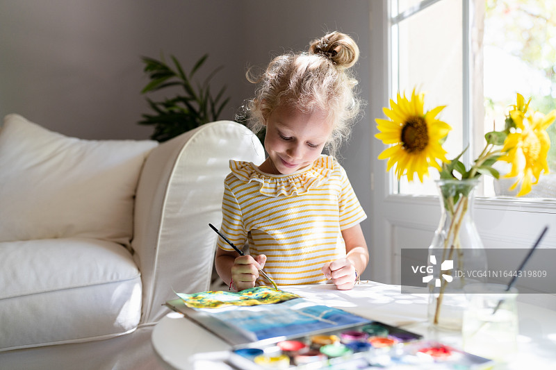 微笑的女孩在家用水彩画风力涡轮机和向日葵田图片素材