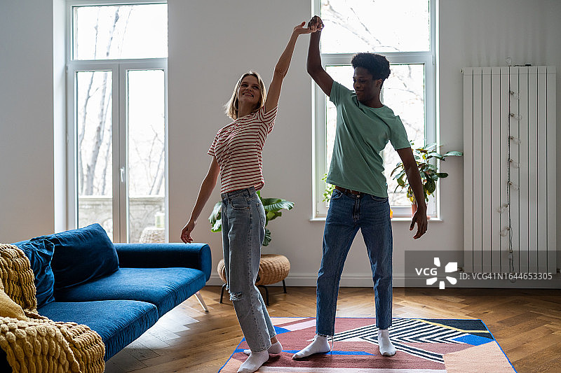 相爱的女朋友在客厅里和非裔美国人男朋友跳舞，庆祝购买新公寓图片素材