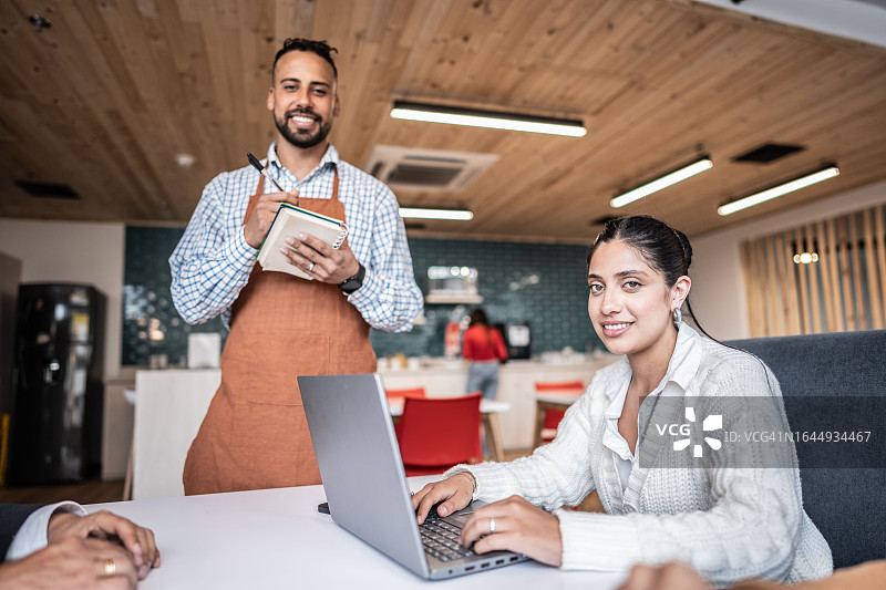 女商人在办公室咖啡厅使用笔记本电脑工作，服务员点餐图片素材