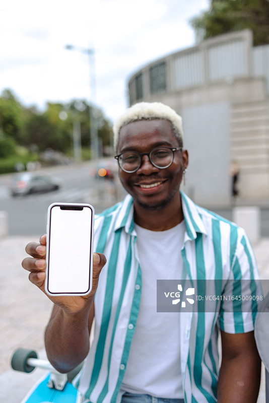 笑容满面的非裔美国男人展示带空白屏幕的智能手机图片素材
