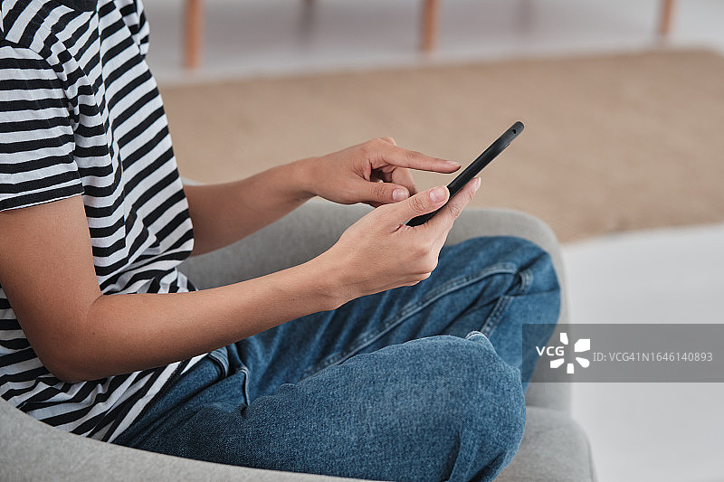 女子在家中使用手机，坐在扶手椅上触摸智能手机屏幕的局部照片图片素材