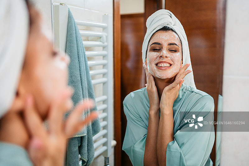 年轻女人在浴室镜子前涂抹面霜图片素材