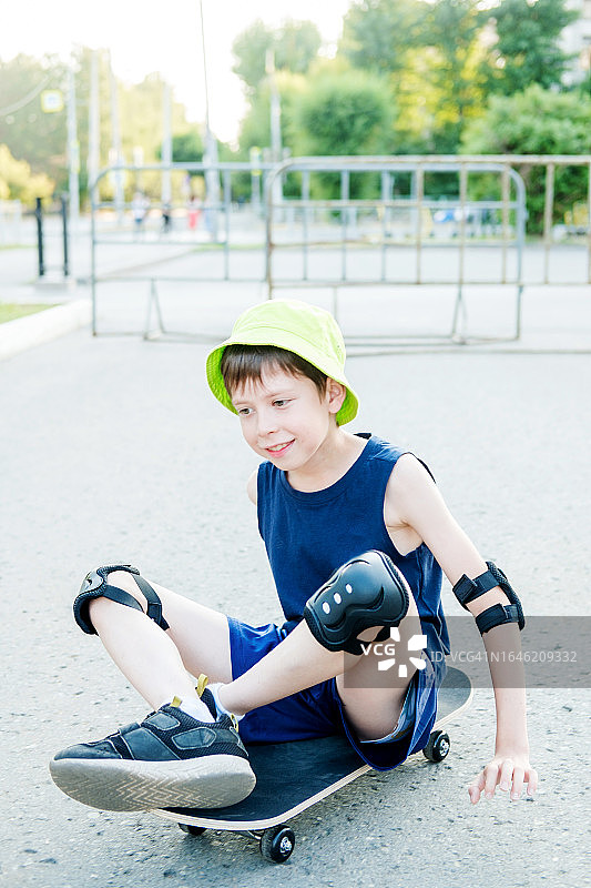 11岁的男孩戴着绿色巴拿马草帽坐在滑板上，背景是城市街道图片素材