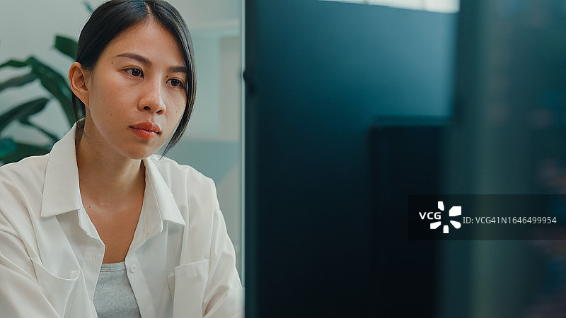 年轻亚洲女性软件开发人员在办公桌前使用电脑编写代码，多屏幕工作特写。程序员开发。图片素材