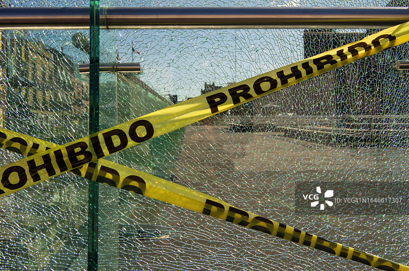 阳台上破碎钢化安全玻璃面板上的西班牙语“Prohibido”塑料警戒带图片素材