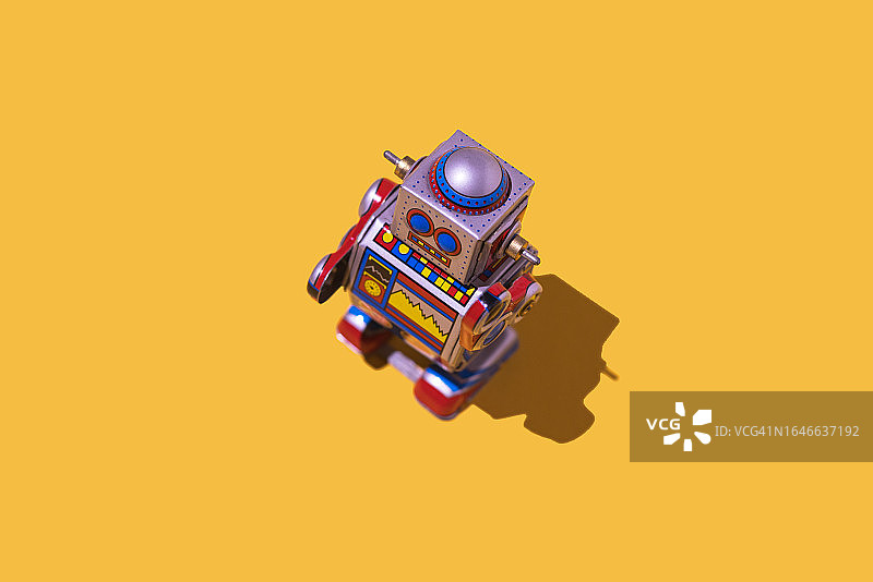 黄色背景上手绘时钟和显示器的复古铁皮玩具机器人。怀旧复古玩具安卓概念图片素材