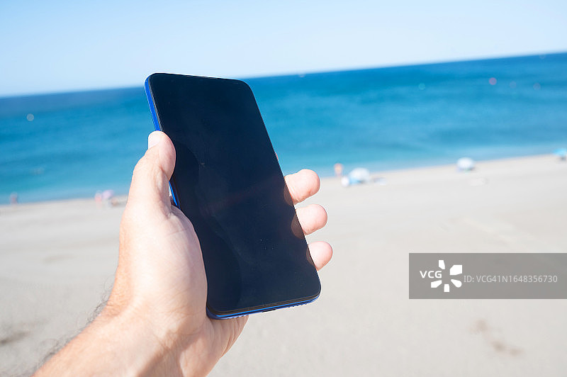 在阳光明媚的海滩边使用智能手机的人图片素材