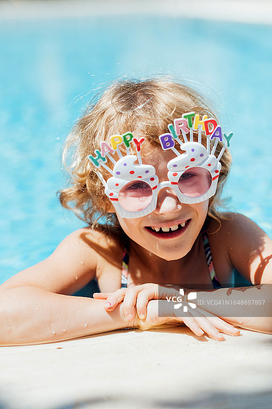 快乐的孩子庆祝生日，戴着生日眼镜的可爱女孩在泳池里游泳，假日和假期概念图片素材