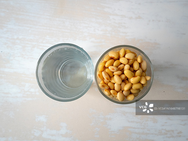 白色桌子上玻璃杯旁浸泡的黄豆图片素材
