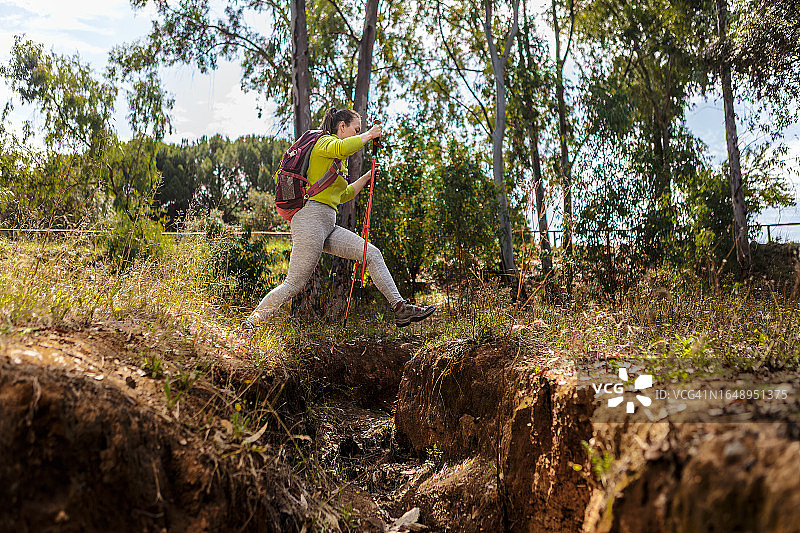 用斯堪的纳维亚滑雪杖跳过溪流的女人图片素材