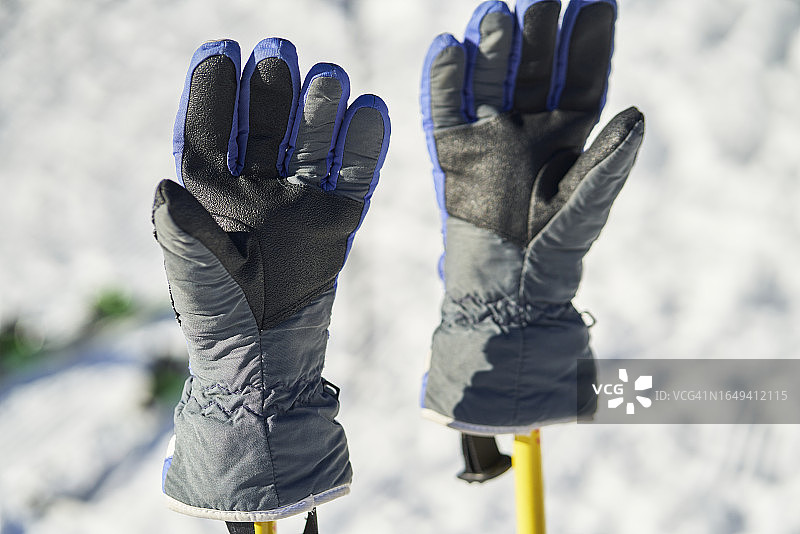 雪地里滑雪杖上的蓝色黑色手套（无人物，正面视角）图片素材