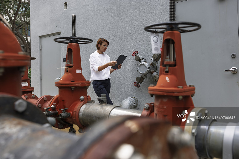 解决供水和损害赔偿问题：女性理赔员使用平板电脑识别户外消防栓的结构脆弱性。选择性聚焦于背景中的女人图片素材