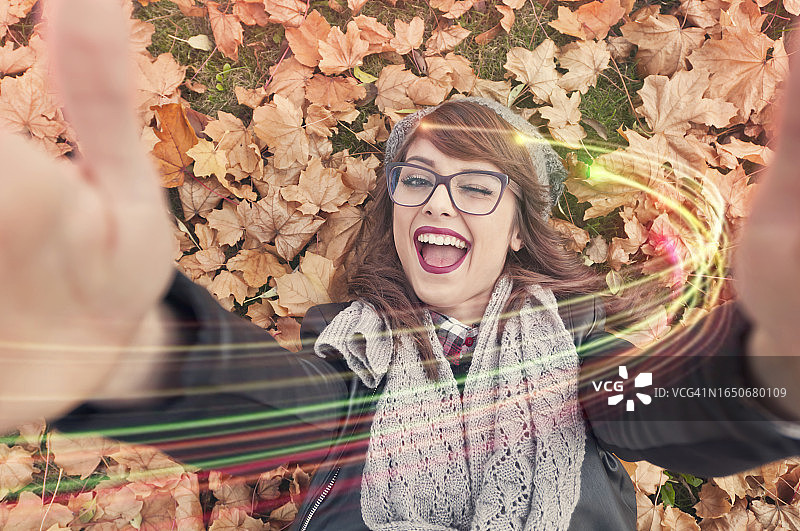 年轻女子躺在秋叶上自拍图片素材