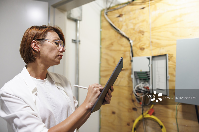 评估大厅中的保险丝盒和电缆：理赔员用平板电脑评估公寓的电气系统图片素材