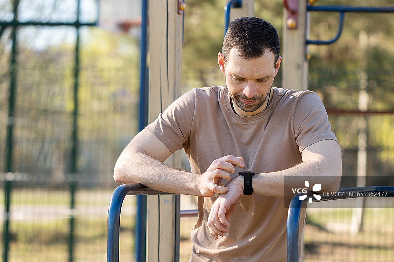 在户外锻炼时查看智能手表上的计时器的健壮男人图片素材