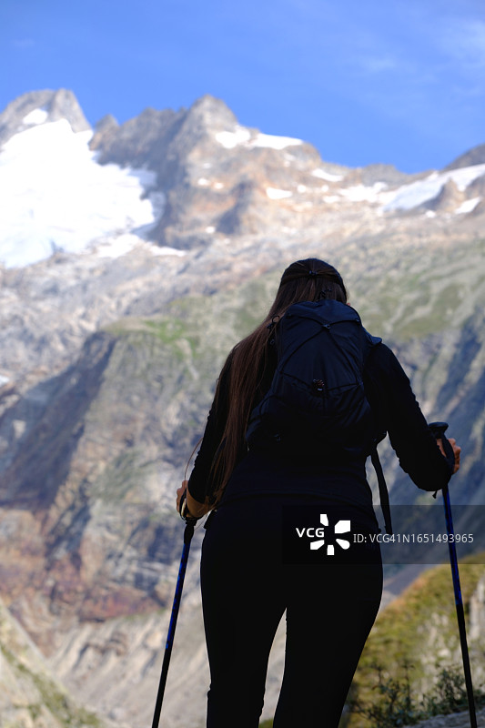 年轻女子借助登山杖行走在山路上，健康的生活方式图片素材