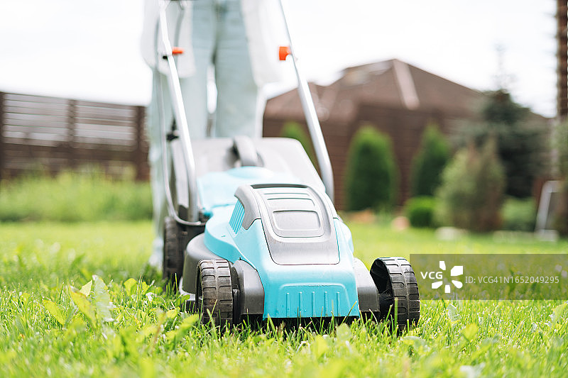 年轻女子在后院用割草机修剪草坪图片素材