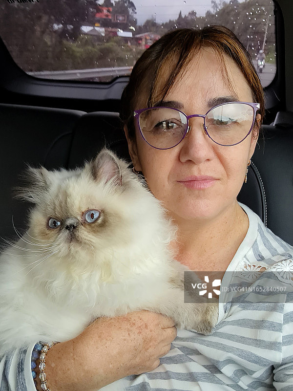 一位中年妇女在汽车后座上抱着猫的自拍照图片素材