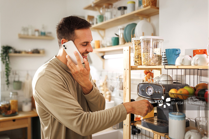 年轻休闲的男人在厨房里一边做咖啡一边打电话图片素材