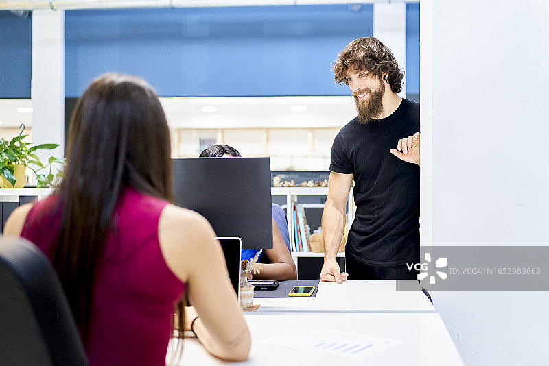 年轻白人女性在办公室里将文件交给老板，同事坐在笔记本电脑前图片素材