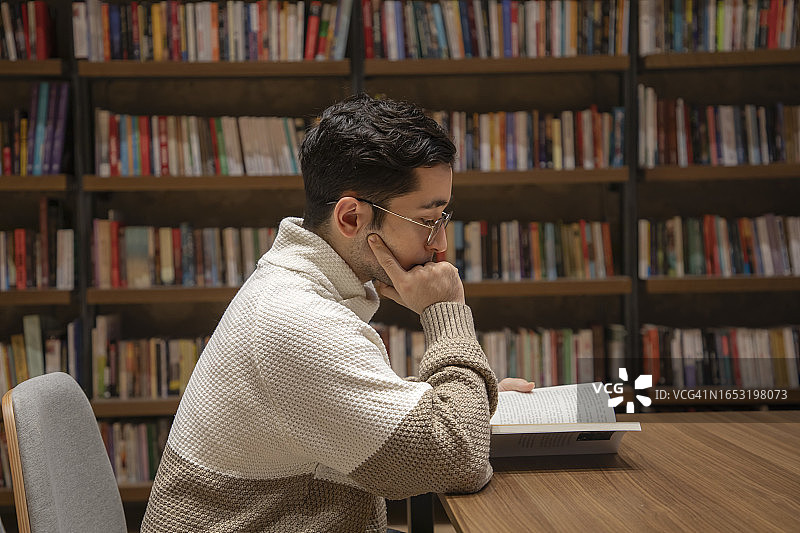 戴眼镜的年轻男子在图书馆里看书图片素材