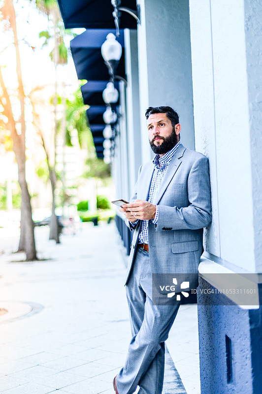 在市区靠着建筑物使用手机的西装商人图片素材