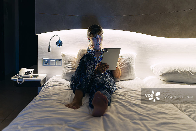 赤脚躺在酒店床上玩平板电脑的女游客（正面视角）图片素材