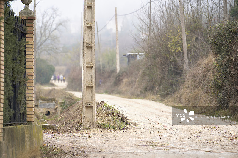 森林中间的泥路，远处有建筑物和行人图片素材