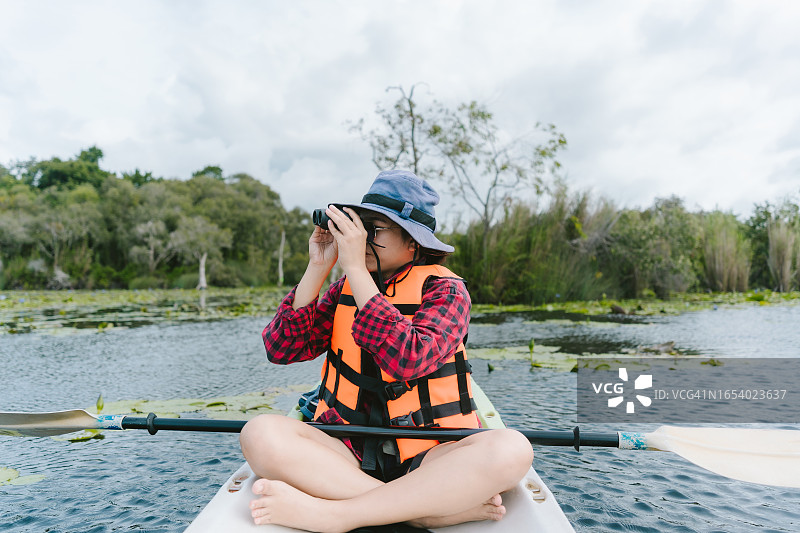 亚洲女孩划船在青色森林和溪流中旅行。冒险和旅行，用双筒望远镜观察自然图片素材