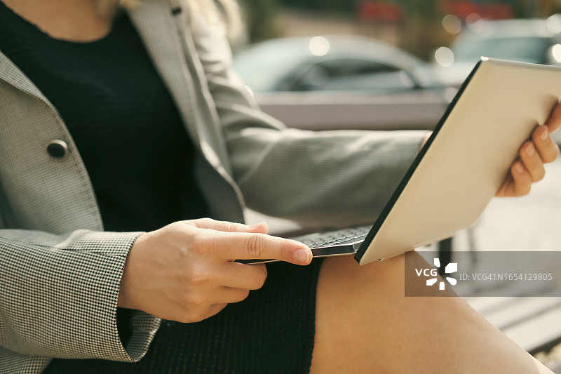 年轻女子坐在长椅上，膝盖上放着超极本图片素材