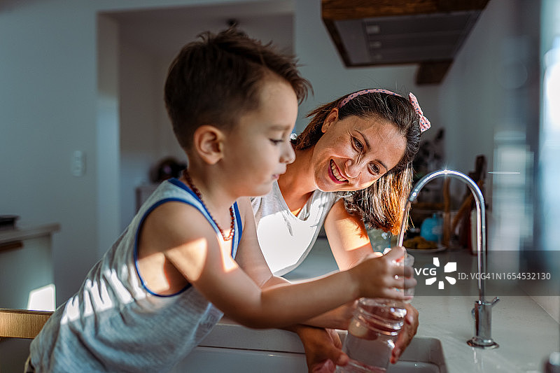 母亲和幼儿从水龙头接过滤水图片素材