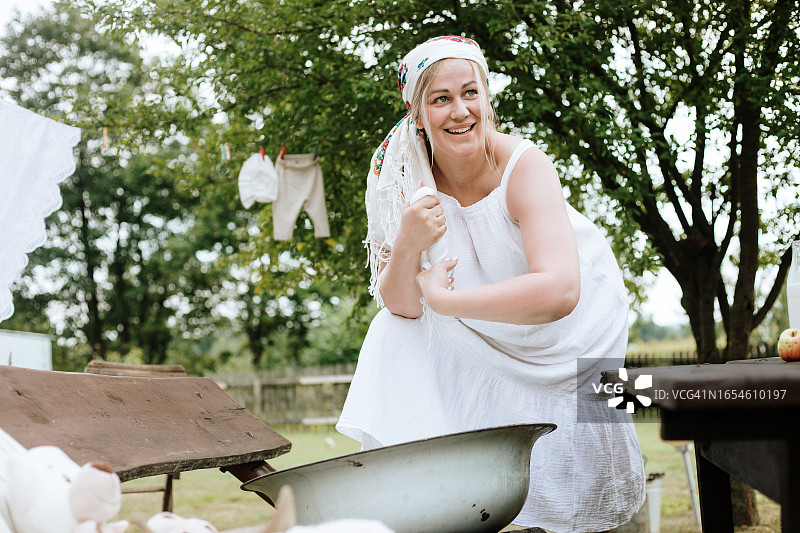 站在乡村，在骨盆里用手洗完衣服后，拧干衣物的微笑孕妇图片素材