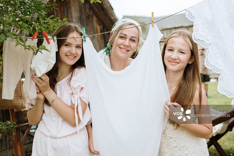 迷人的准妈妈和可爱的女儿们站在晾衣绳后面，对着镜头露出灿烂的笑容图片素材