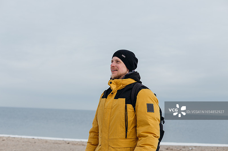 戴黑帽子和黄色夹克的微笑青年在沙滩上图片素材