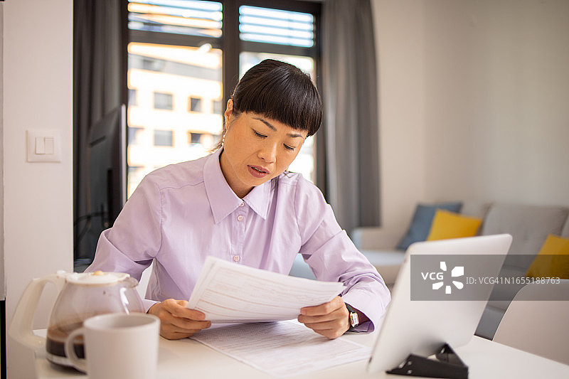 年轻女子使用计算器，同时通过账单和家庭财务图片素材