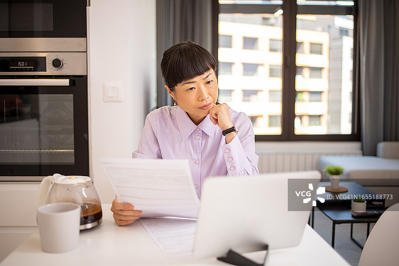 年轻女子使用计算器，同时通过账单和家庭财务图片素材