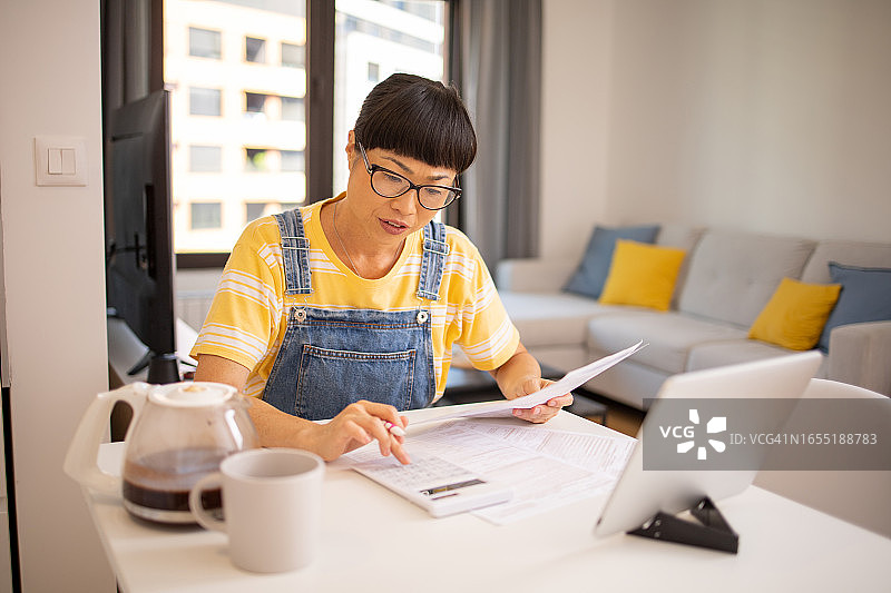 年轻女子使用计算器，同时通过账单和家庭财务图片素材