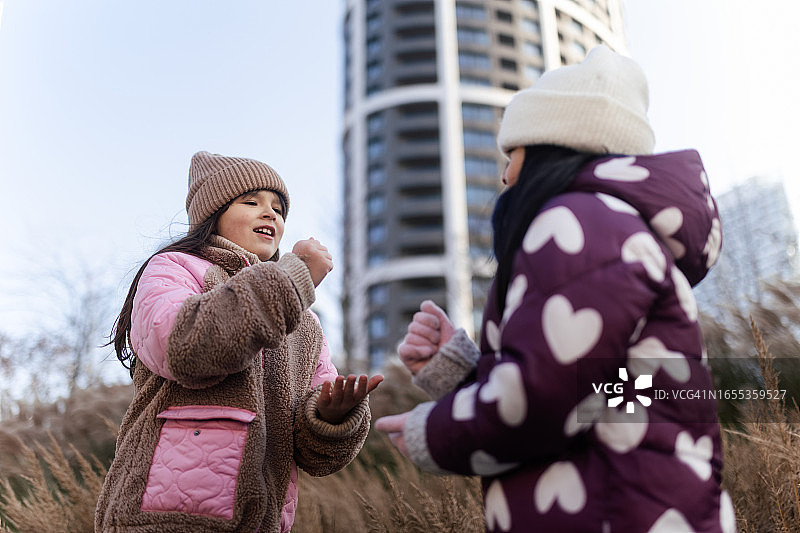两个漂亮小女孩在城市草地上玩石头剪刀布游戏图片素材