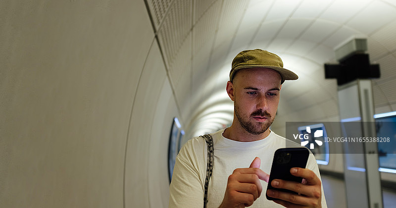 戴帽子的年轻男人在地铁里用手机导航图片素材